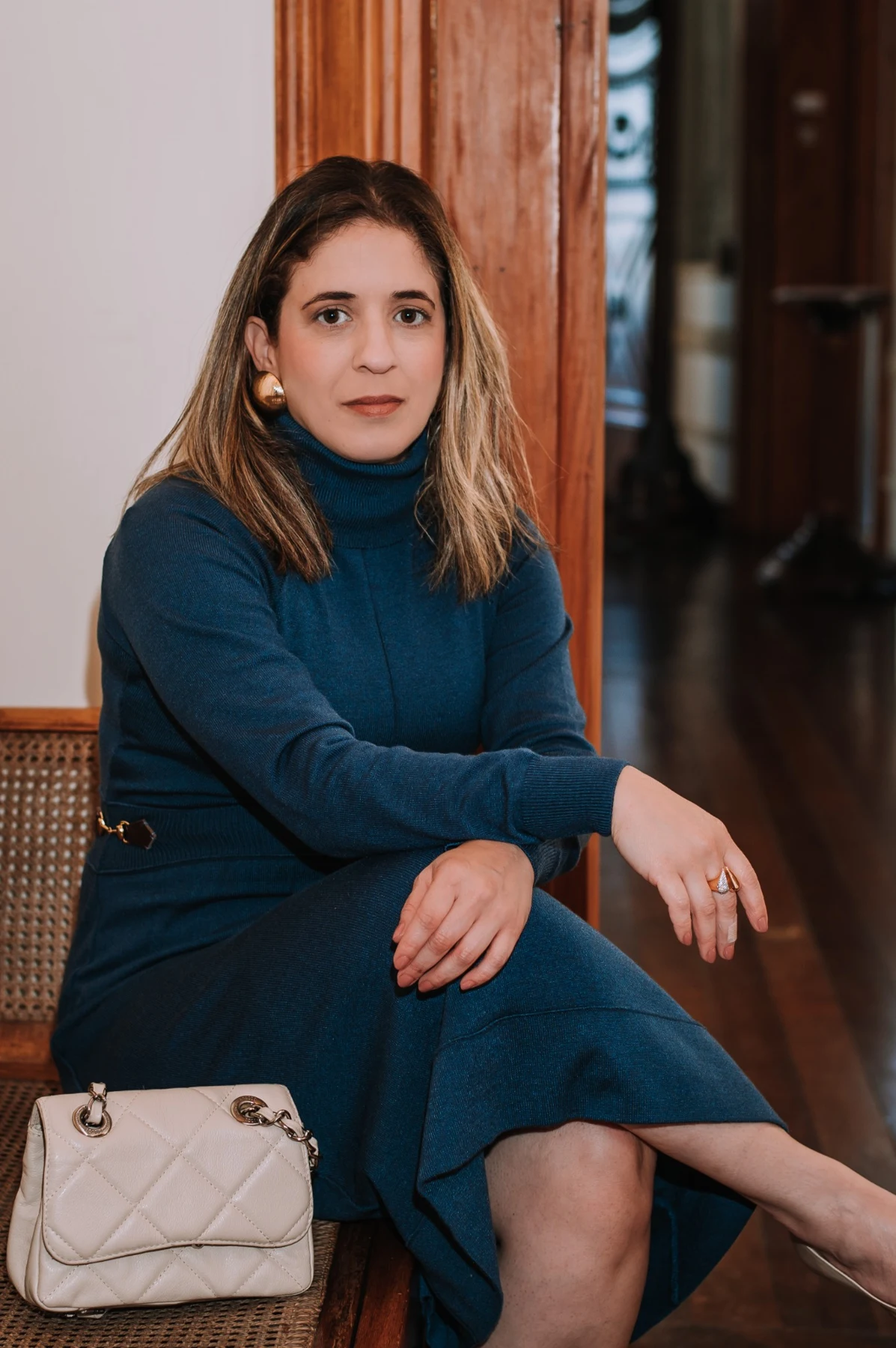 Cilene Agostinho sentada, usando um vestido azul e segurando uma bolsa